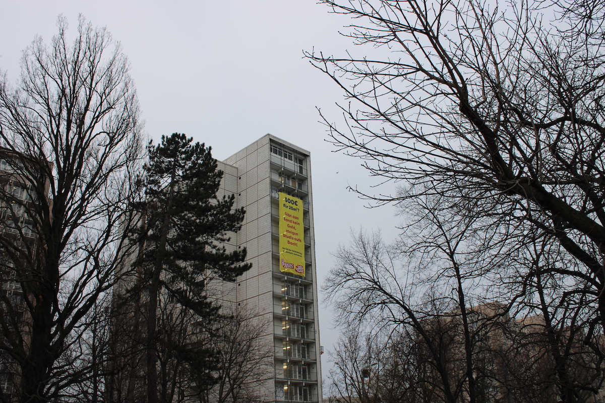 Gerokstraße 38 mit Banner mit der Aufschrift „Wenn das Land nicht zahlt, steigen Studis aufs Dach“ aus der Ferne
